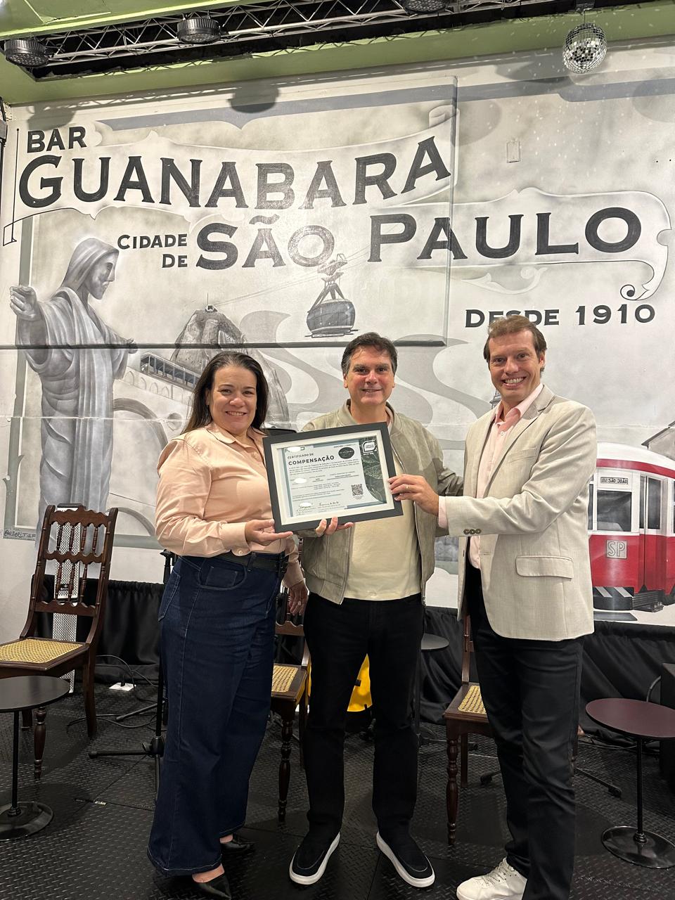 Entrega do certificado de compensação de emissões no Bar Guanabara, São Paulo, com documentação do projeto visível
